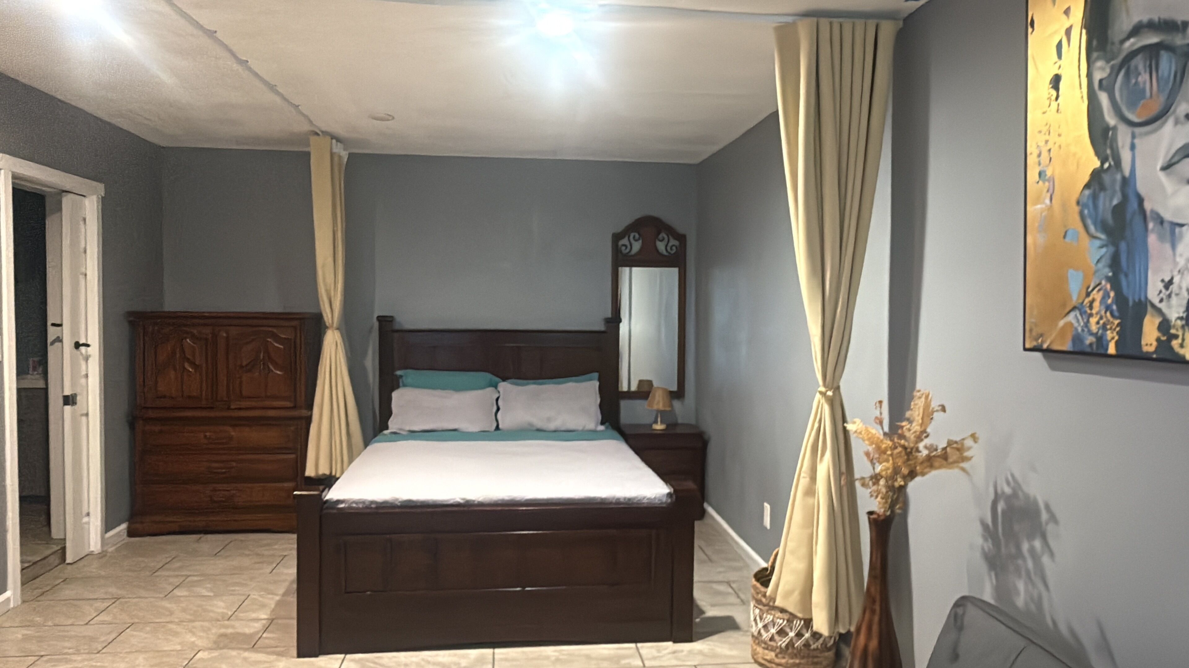 A bedroom with a wooden bed, a nightstand, a mirror, and a painting on the wall.