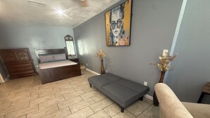 Un dormitorio con cama, sofá, una mesita, un espejo y un cuadro en la pared.