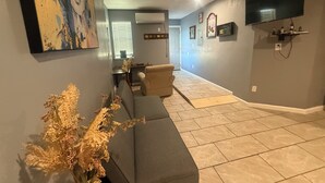 Una sala de estar con un sofá gris, un ventilador de techo, un televisor de pantalla plana y un comedor con mesa y sillas.