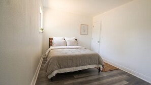 Ein schmales Zimmer mit einem Bett, einer Tür und einem kleinen Fenster.