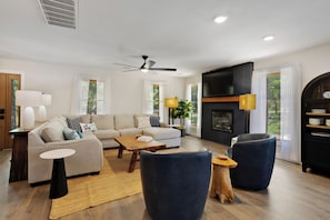 A modern living room with a sofa, coffee table, chairs, a fireplace, and a television.