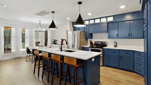 Una cocina moderna con una isla central, taburetes de bar y muebles azules.