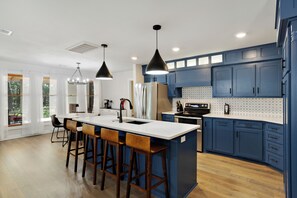 Een moderne keuken met een centraal eiland, barstoelen en blauwe kastjes.