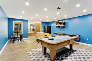 Een pooltafel met een blauwe viltkleed, een bar met krukken, en een houten vloer.