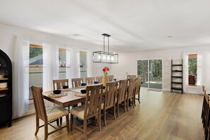 Een eetruimte met een lange houten tafel, stoelen en een hanglamp.
