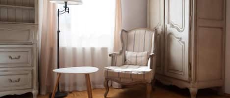 Una habitación con suelo de madera, una mesa blanca, un sillón a rayas, una lámpara y un armario blanco.