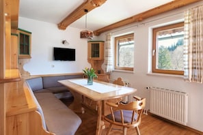 A cozy room with a wooden bench, a dining table, and a TV mounted on the wall.