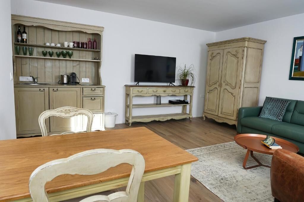 A living room with a wooden dining table, a green sofa, a television, and a cabinet with kitchenware.