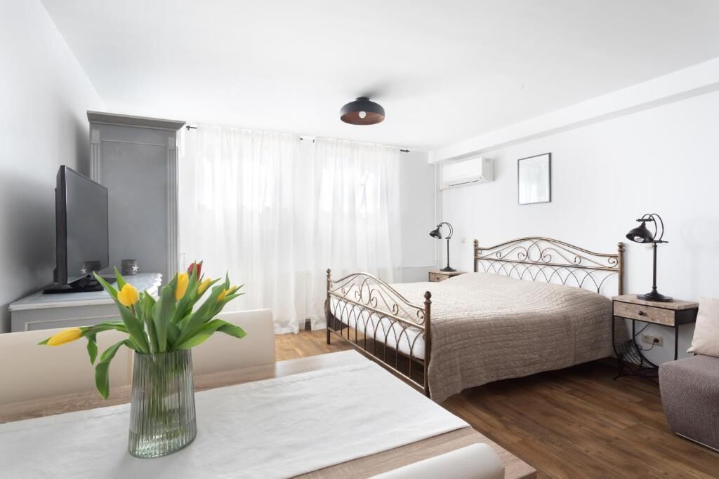 A bedroom with a bed, bedside tables, a TV, a lamp, and a vase with flowers.
