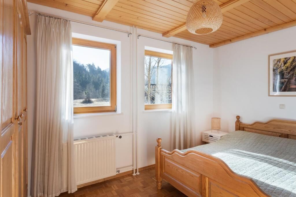 A bedroom with a wooden bed, a nightstand, a lamp, and a window with a view of trees.