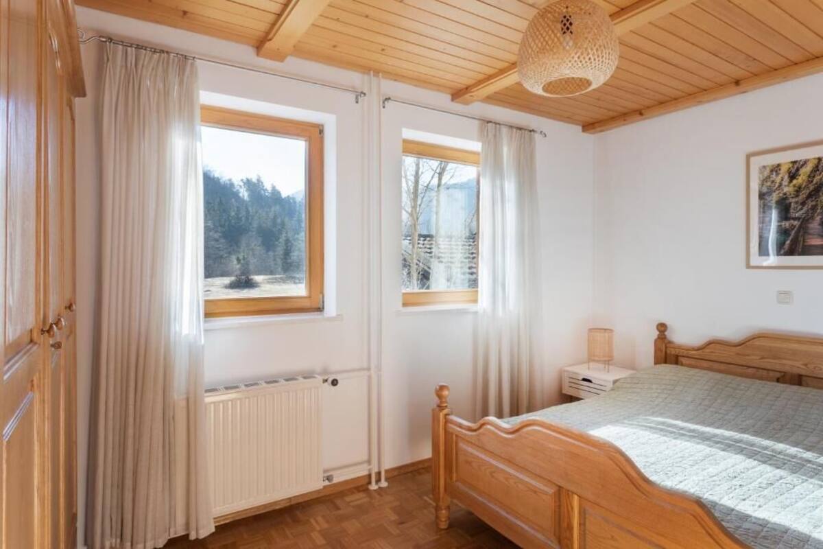 A bedroom with a wooden bed, a nightstand, a lamp, and a window with a view of trees.
