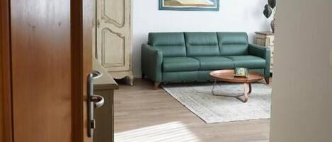 A room with a wooden floor, a green sofa, a small table, and a cabinet.
