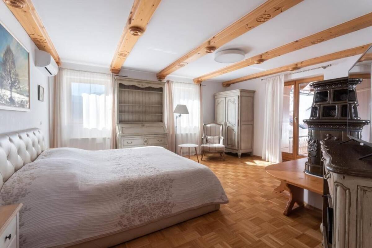 A bedroom with a large bed, wooden beams, a dresser, and a stove.