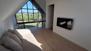 Une pièce spacieuse dotée d’une grande fenêtre, d’un téléviseur à écran plat fixé au mur et d’un plancher en bois.