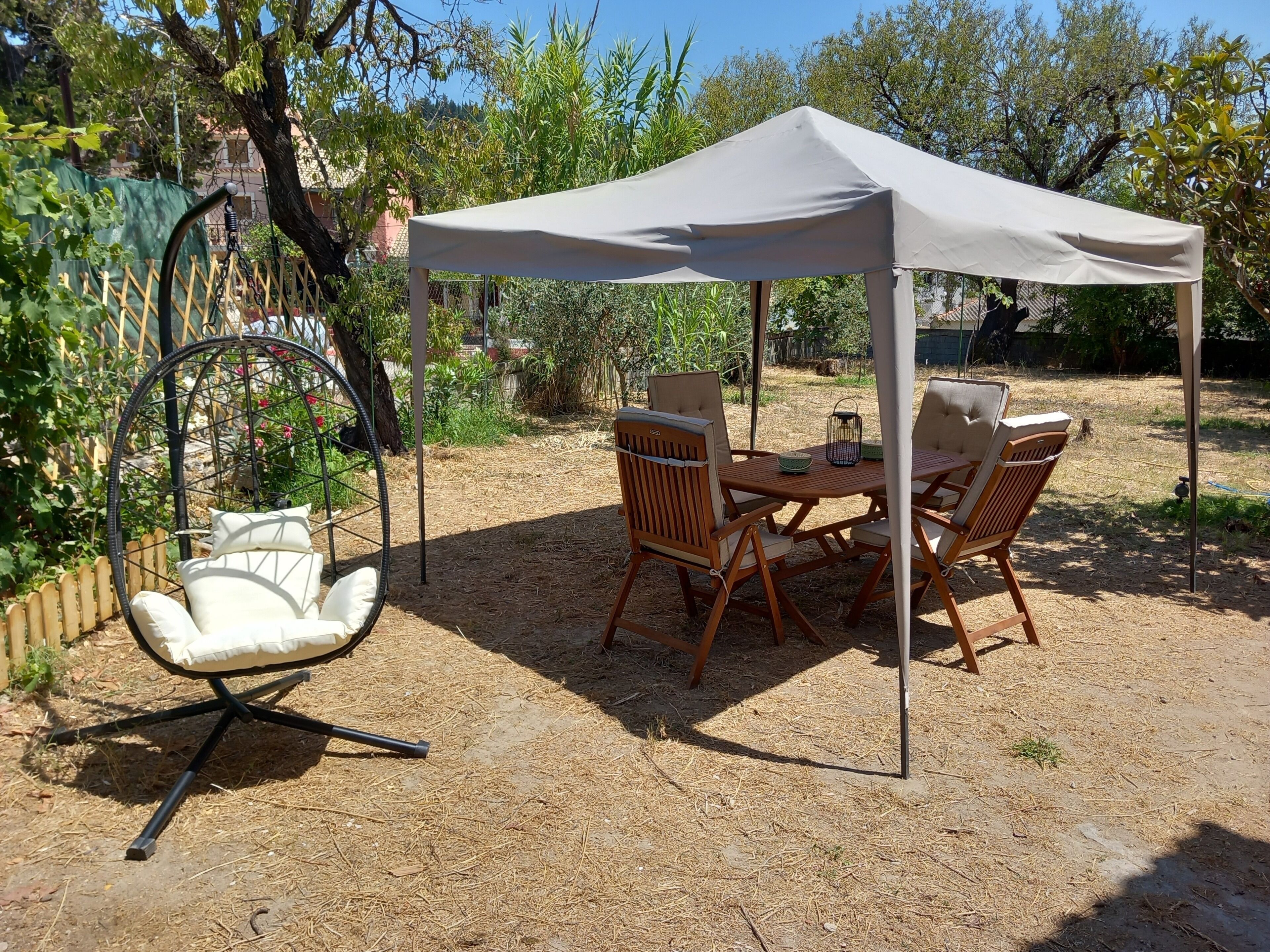 Un espace extérieur aménagé en terrasse, avec une table ronde et des chaises, un fauteuil suspendu et un auvent.