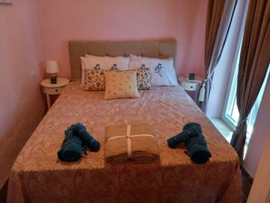 Habitació d'hotel amb un llit, almoines, una taula de nit, una làmpada i una finestra amb cortines.