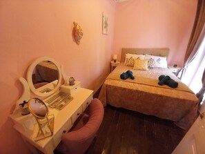 A hotel room with a bed, bedside table, mirror, and a pink bench. - Belvedere di Van D'oro 1886 (Peroulades)