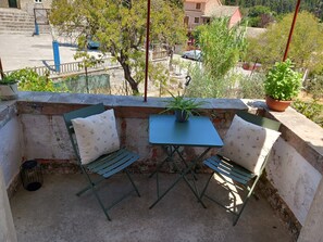 Un balcón con una pequeña mesa, dos sillas, una planta en maceta y vistas a la calle y edificios.