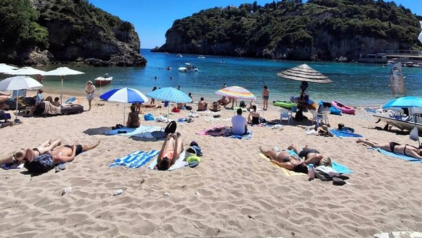 Una playa con gente tomando el sol, sombrillas y barcos.