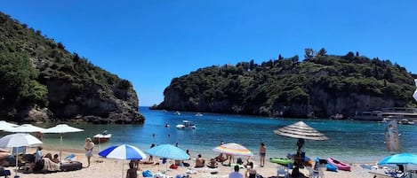 Une plage où l’on voit des gens se prélasser au soleil, des parasols et des bateaux.
