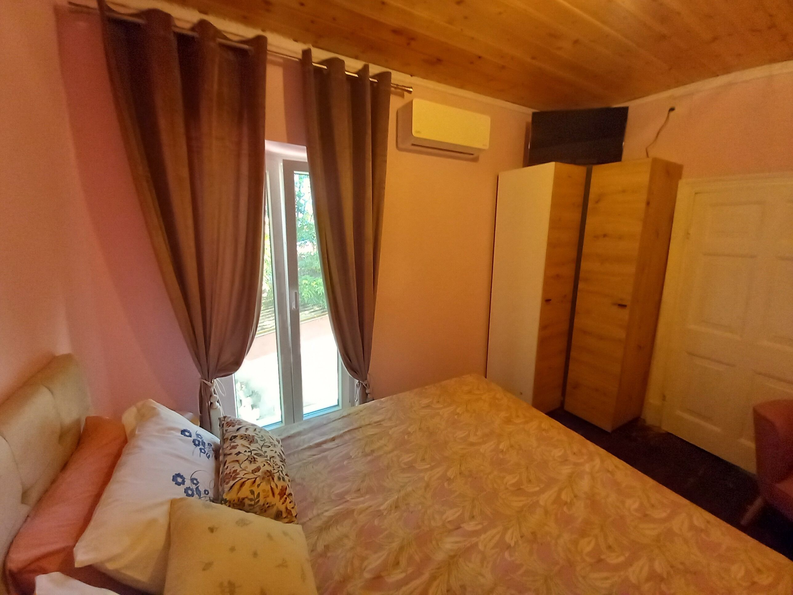 A bedroom with a bed, curtains, a wardrobe, and a door.