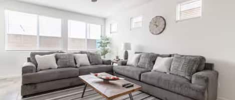 A living room with a sofa set, a coffee table, a ceiling fan, and a clock on the wall.