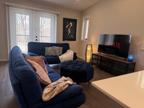 Ein Wohnzimmer mit einem blauen Sofa, einem Hocker und einem Fernseher, der 'NETFLIX' zeigt.