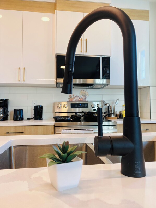 A modern kitchen with white cabinets, a black faucet, a microwave, and a stove. - *Brand New BUDGET*Sleep 6*Downtown 5 MINS* (Edmonton)