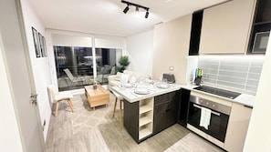 Cozinha moderna com fogão embutido, área de jantar com mesa posta para dois e uma grande janela com vista para a rua.