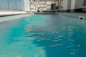 Una piscina con agua azul cristalina, una escalera de piscina y una planta en maceta cerca del borde.