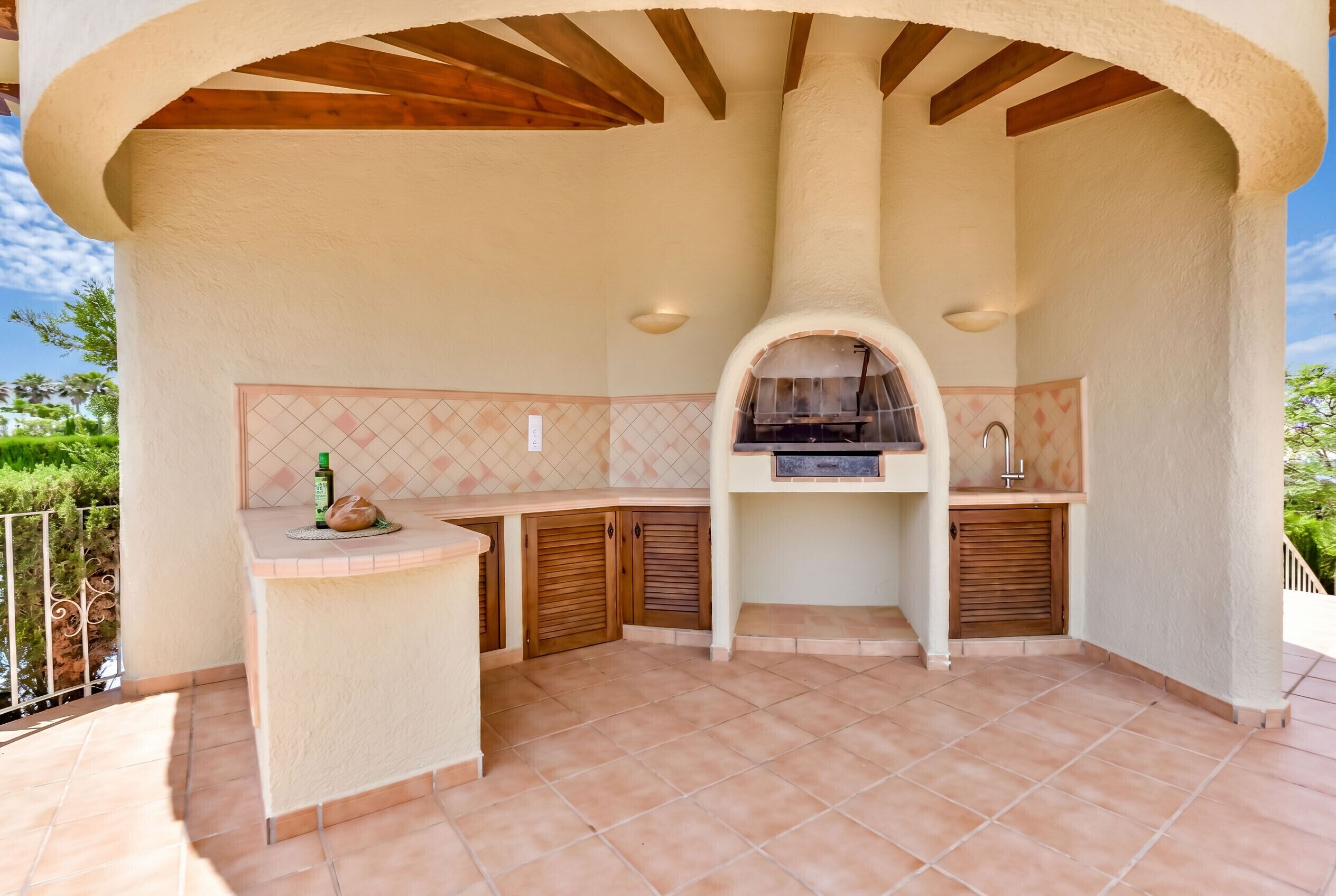 An outdoor kitchen with a chimney, wooden cabinets, and a tiled backsplash.