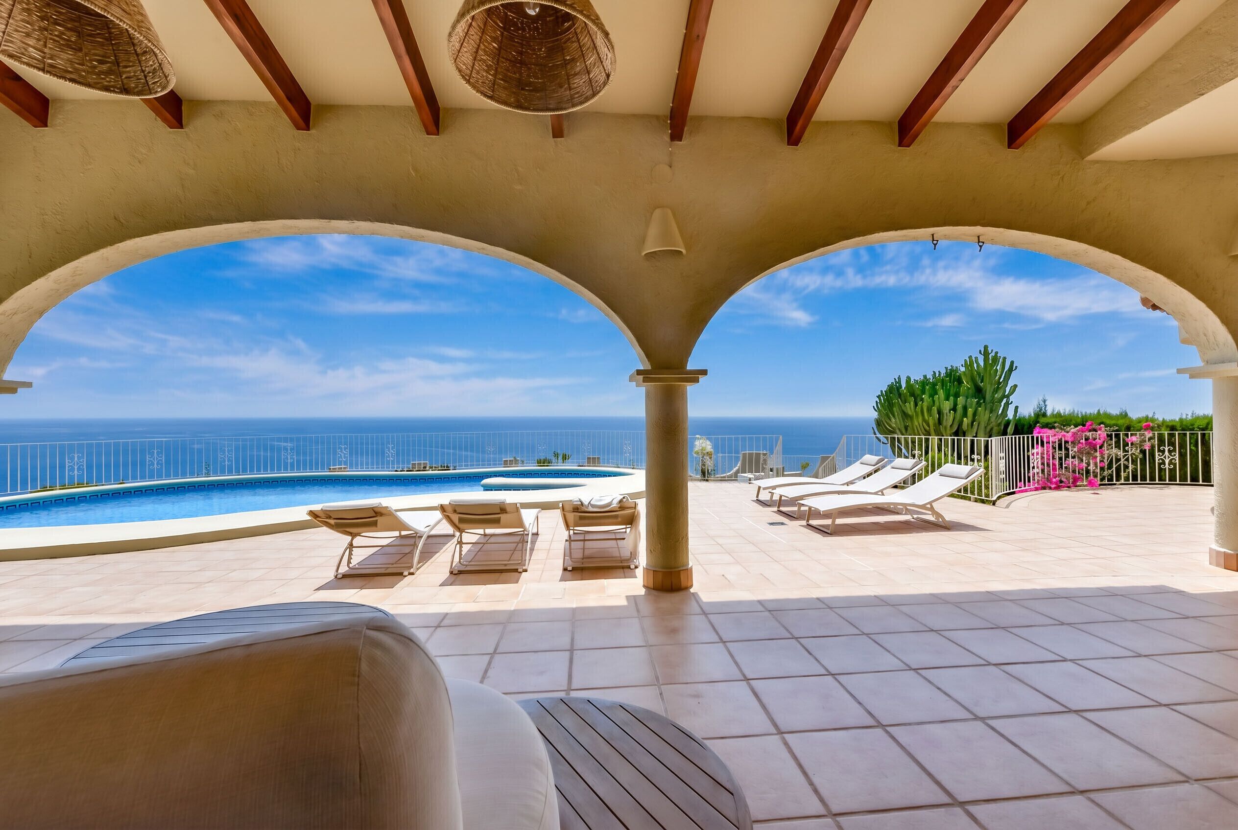 Un área junto a la piscina con sillones, vista al mar y una pérgola.