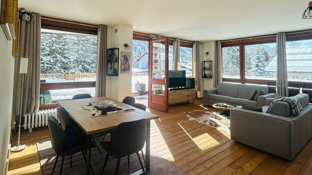 A spacious living area with a dining table, sofa, and large windows offering a view of a snowy landscape. - Pragelato Weekend (pragelato)