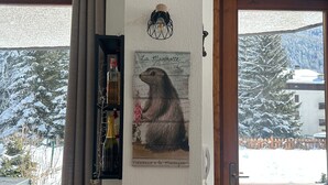A room with a wooden door, a wall-mounted light fixture, a framed picture of a marmot, and a view of snow-covered trees. - Pragelato Weekend (pragelato)