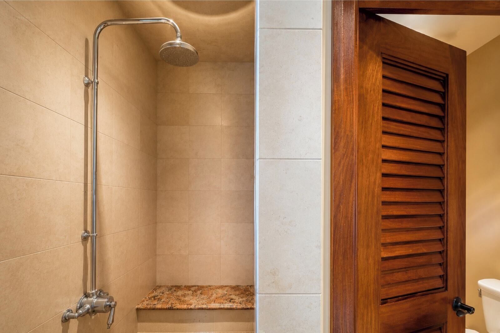 A shower with a handheld showerhead, a wooden door with horizontal slats, and a tiled wall.