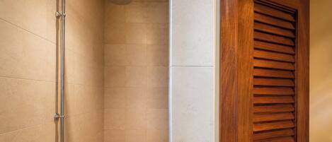 Eine Dusche mit Duschbrause, eine Holztür mit Lamellen und eine geflieste Wand.