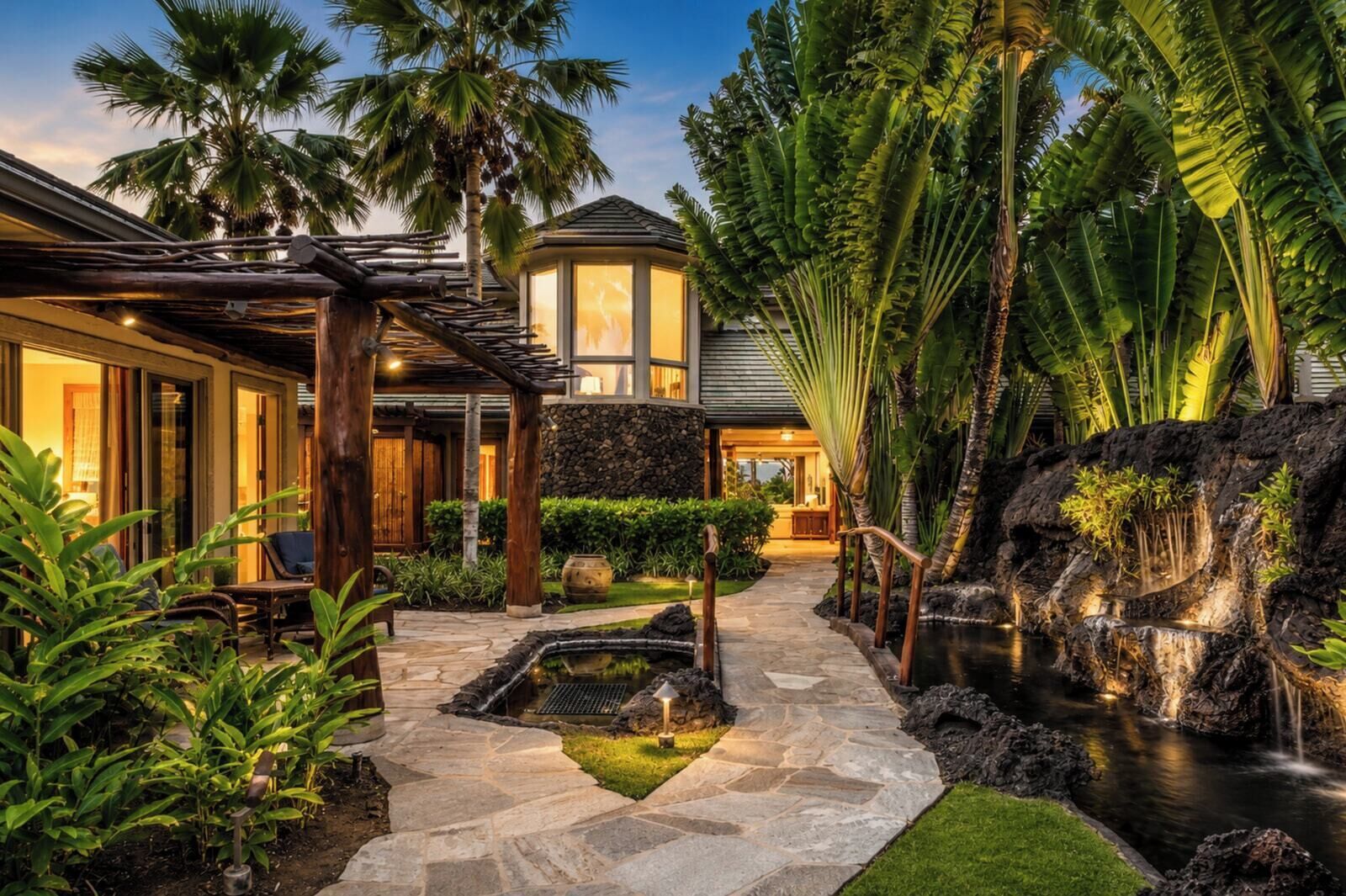 A tropical resort with a stone pathway, a small pond, and lush greenery.