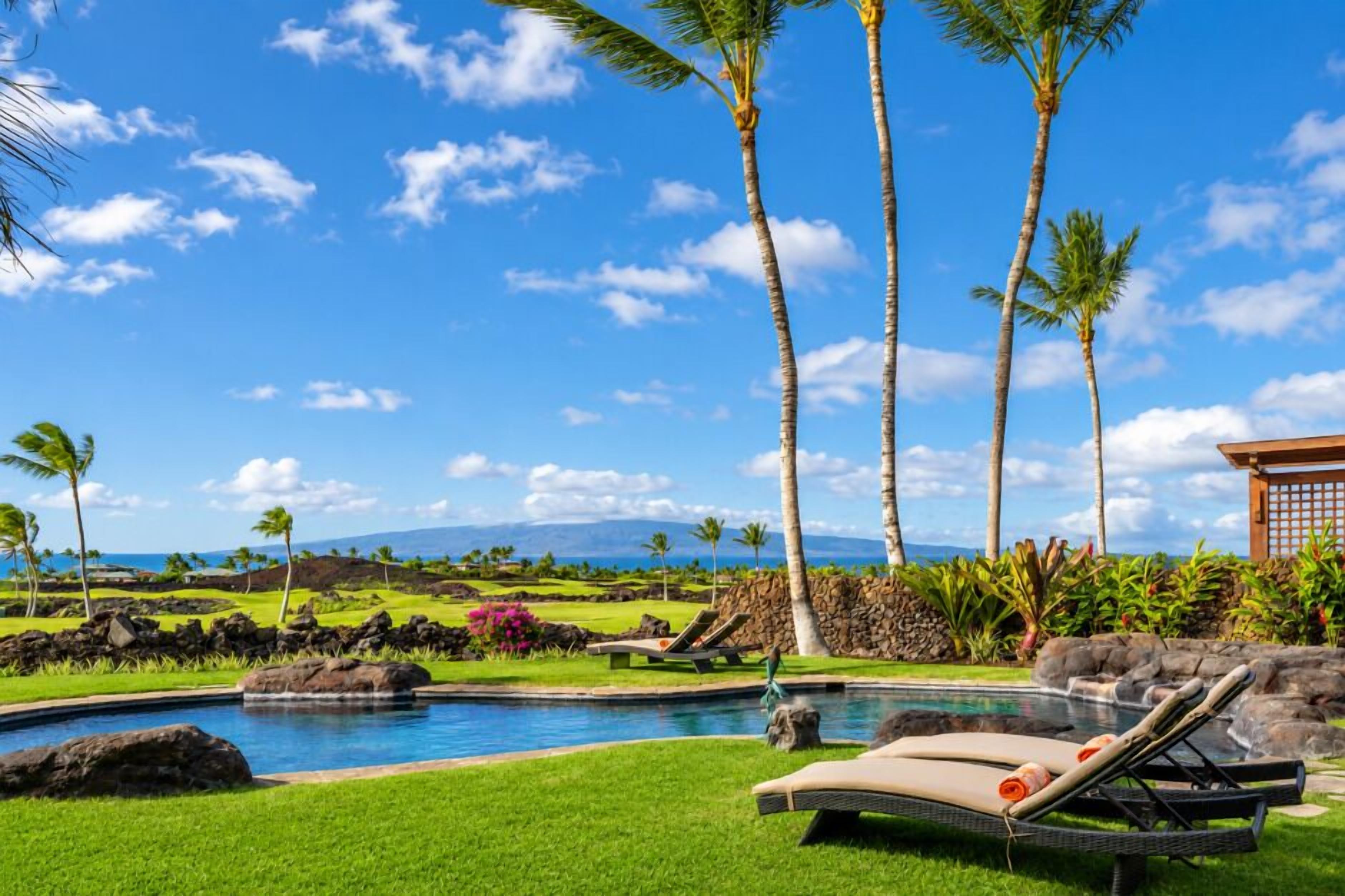 A pool area with lounge chairs, palm trees, and a view of the ocean.