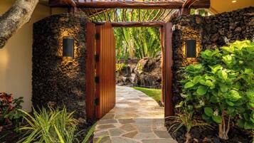 A stone pathway leading to a wooden gate with a tropical garden on either side.