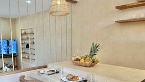 A modern kitchen with a marble countertop, wooden stools, a fruit basket, and a hanging light fixture. - COCAY PI 2219, Hideaway, Pet Friendly, Plunge Pool (Tulum)