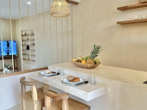 Eine moderne Küche mit Marmorarbeitsplatte, Holzstühlen, einer Obstschale und einer Hängeleuchte.