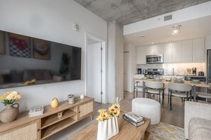 Ein modernes Wohnzimmer mit Flachbildfernseher, einem Holz-Nachttisch und einem Essbereich mit Küche im Hintergrund.
