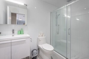 Un bagno moderno con cabina doccia in vetro, un water bianco e un lavandino con specchio sopra.