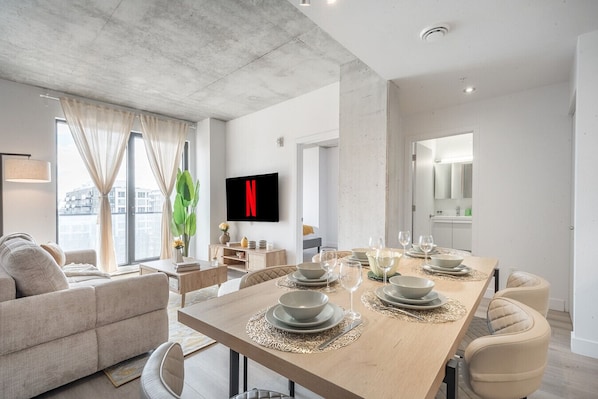 A modern living room with a dining area, a flat-screen TV, and a view of the city. - Prime Old Port Stay | Gym and Parking (Montreal)