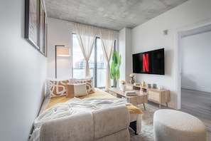 A modern bedroom with a bed, bedside table, TV, and large windows. - Prime Old Port Stay | Gym and Parking (Montreal)