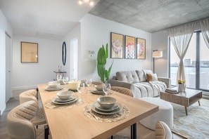 A modern living room with a dining area, a sofa, a coffee table, and a large window with curtains. - Prime Old Port Stay | Gym and Parking (Montreal)