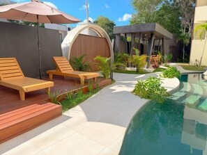 A modern outdoor pool area with wooden lounge chairs, a covered seating area, and a curved pool edge. - Modern Swim-Up Studio by the Pool - Mizu 20 (Tulum)