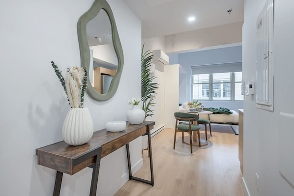 Un intérieur moderne avec une console en bois, un miroir et un coin repas agrémenté d’une chaise verte.
