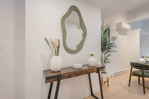 Un salon moderne avec une console en bois, un miroir vert et une plante en pot.