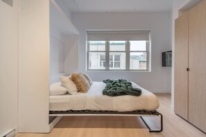 Ein kleines Zimmer mit Bett, Fenster und Kleiderschrank.